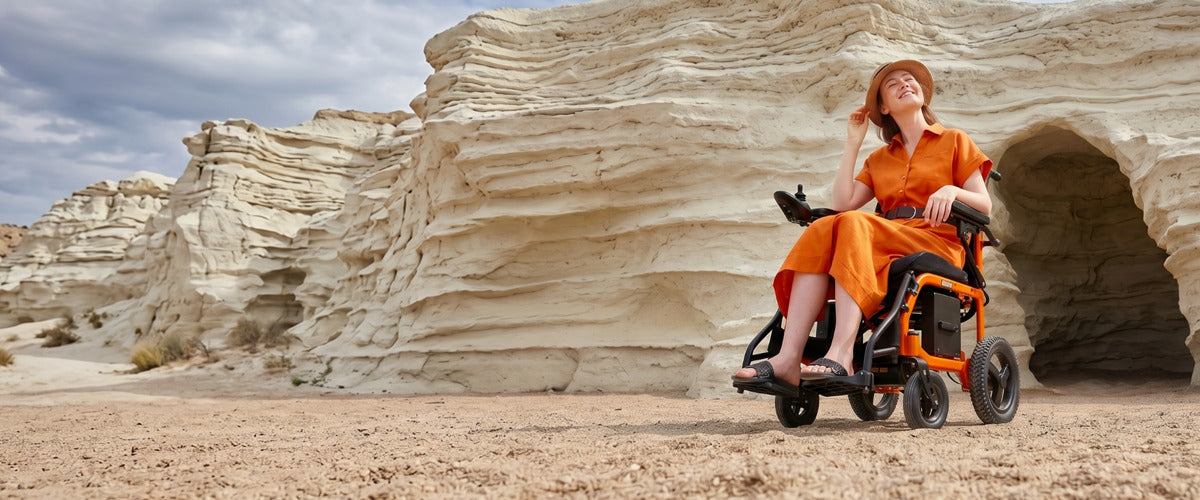 Elektrischer Rollstuhl für Outdoor-Nutzung, Frau im faltbaren E-Rollstuhl in einer natürlichen Felslandschaft, barrierefreie Mobilität und Reisen.
